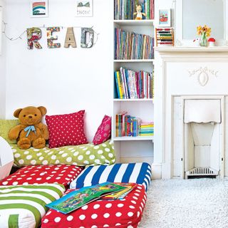white kids' bedroom with fireplace, bookshelves and pillows on the floor