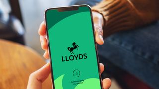 A hand holding a phone showing the Lloyds bank app