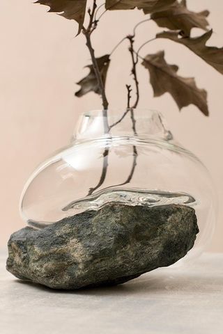 A clear glass vase that's blown around the rock in green and black tones. There are tree branches in the vase.