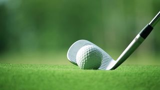 Close up of golf ball on grass, in front of golf club head