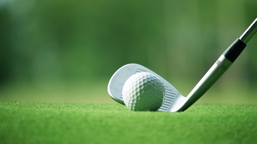 Close up of golf ball on grass, in front of golf club head