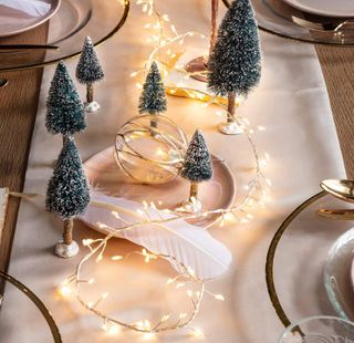 A Christmas-themed dining table with fairy lights and miniature tree decor