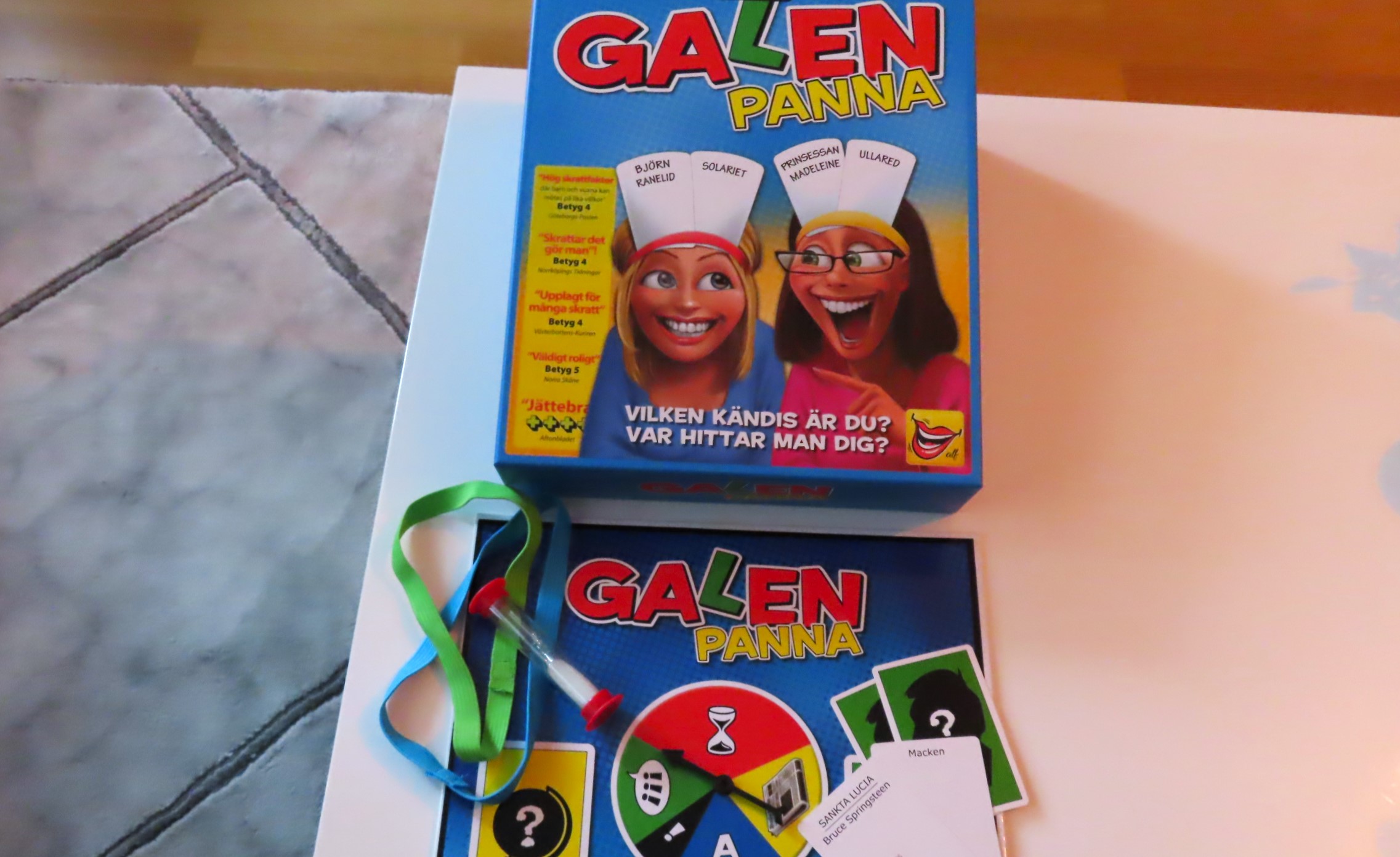 Galenpanna-spelet ligger framplockat på ett vitt vardagsrumsbord bredvid sin tillhörande förpackning.
