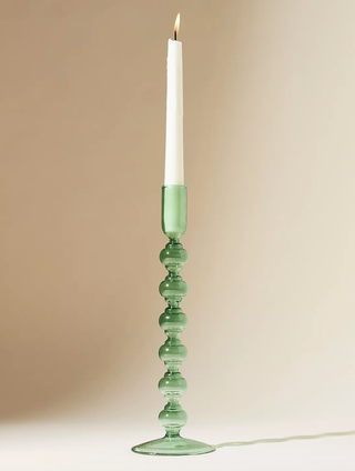 green glass candlestick with a candle on a table