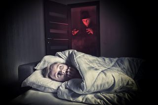 Scared boy lying in the bed while the masked stranger standing in a doorway.