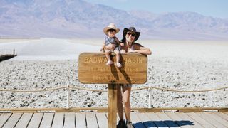 Woman and baby posing with sign at Badwater, Death Valley National Park