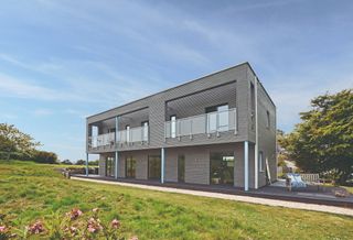 A contemporary new build home with grey timber cladding on an expansive green lawn 