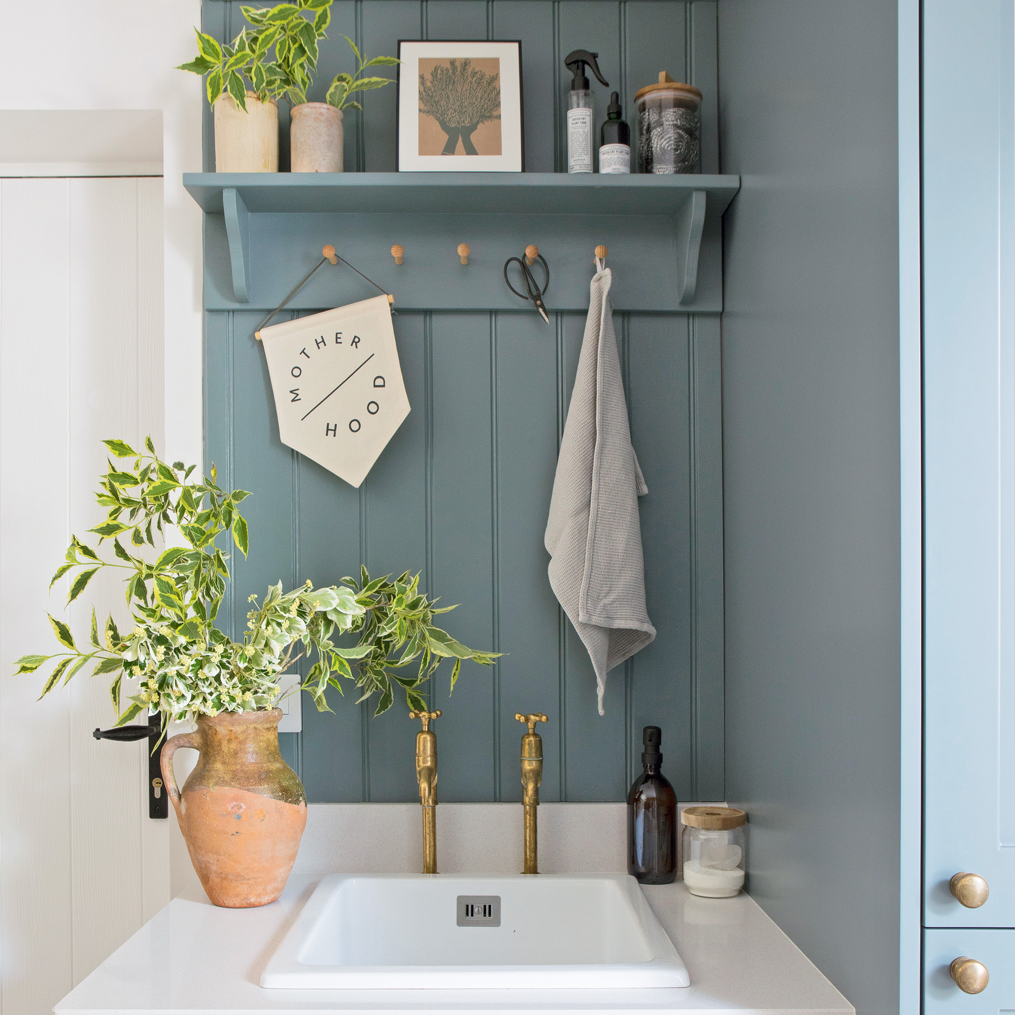 country cottage utility room sink with brass taps, open shelving and blue tongue and groove panelling