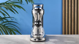 a silver drip brew coffee maker with a 10 cup capacity is photographed against a blue background