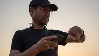 man pictured checking his smartwatch while outside with headphones around his neck, as if taking a break from exercise