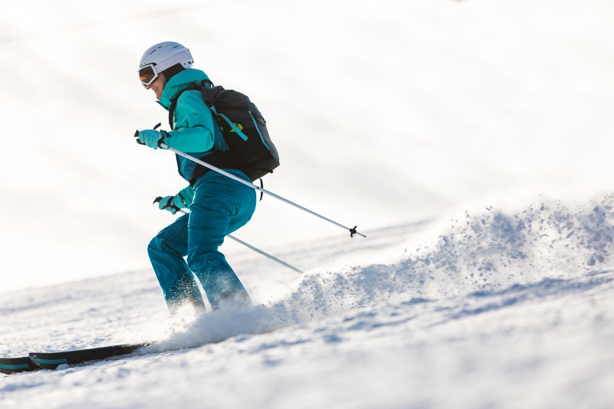 A person wearing blue pants, a blue coat, and a white helmet skiing down a mountain