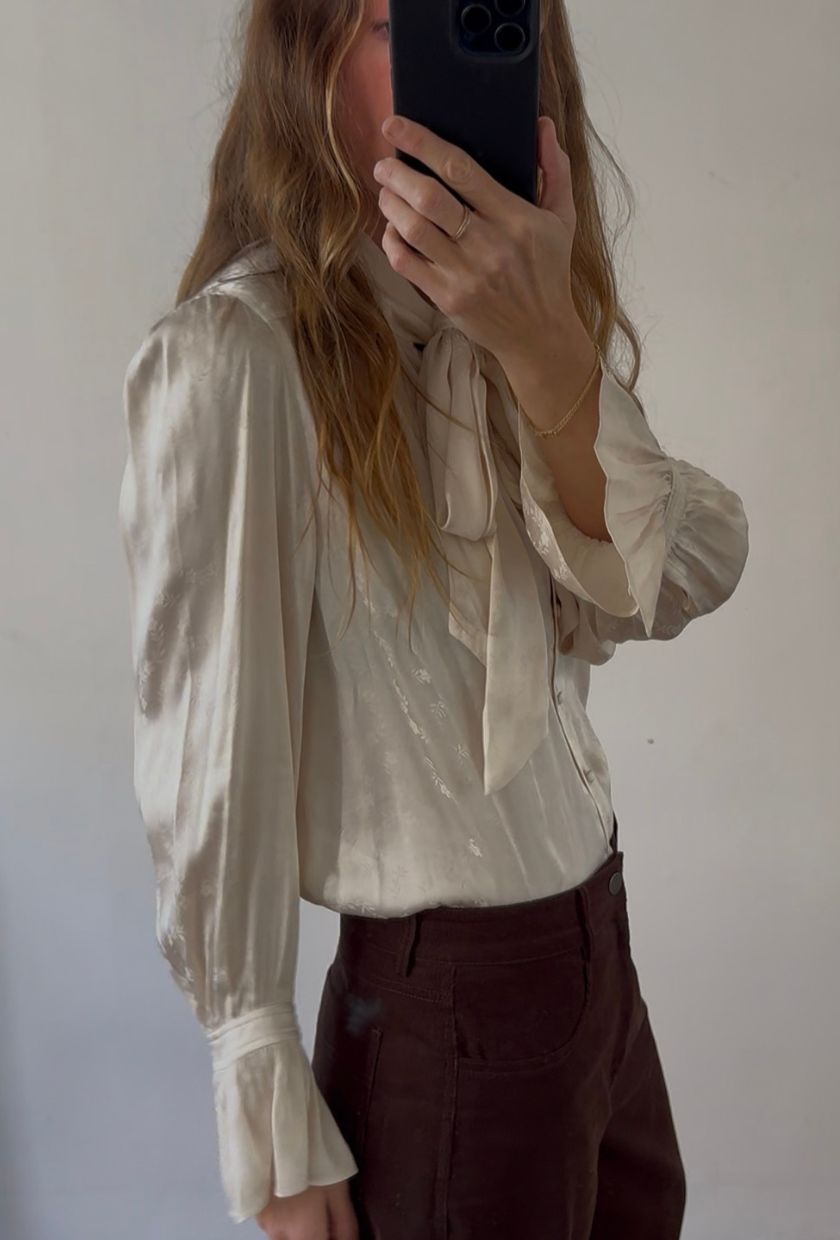 Angie wears a white blouse and brown trousers