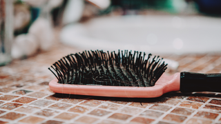 Light pink hairbrush lying face up on a bathroom counter next to white enamel sink