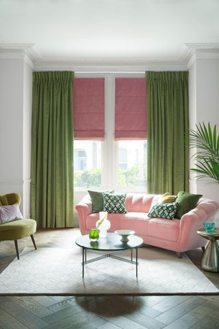 A living room with a pink sofa, green velvet curtains and a pink roman blind