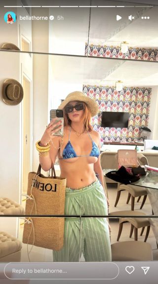 Bella Thorne taking a mirror selfie in a small blue bikini and green pants.