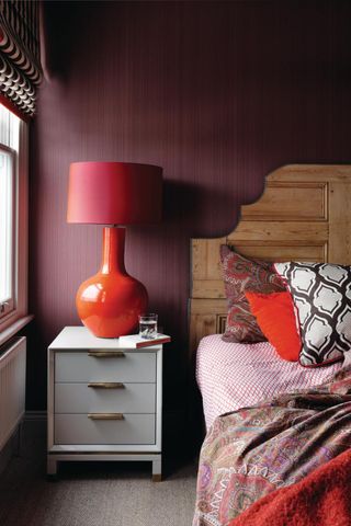 A burgundy bedroom with a red lamp on the side table
