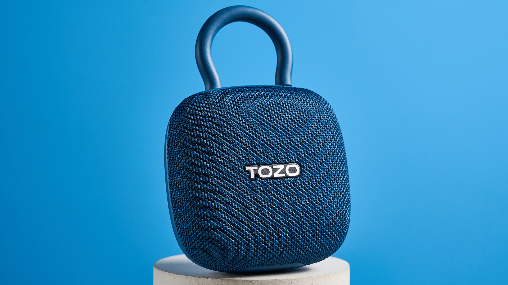 Tozo PE1 speaker in blue with built-in clip photographed on a blue background.
