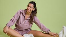 Rachael Sacerdoti sits in a loose workout jumper, shorts and shoes, stretching and smiling.