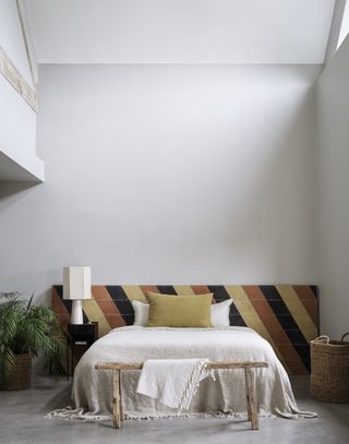 pale gray and white bedroom with tiled headboard, gray floor tiles, vaulted ceiling, rustic bench, black side table, baskets