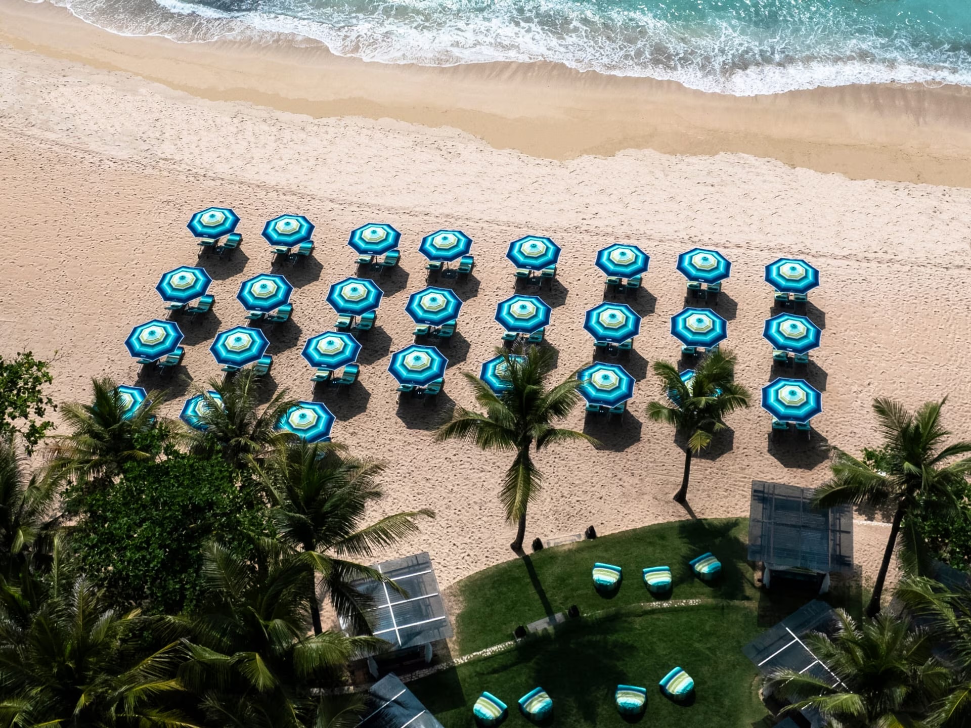 Photograph of turquoise and emerald parasols on a sandy beach