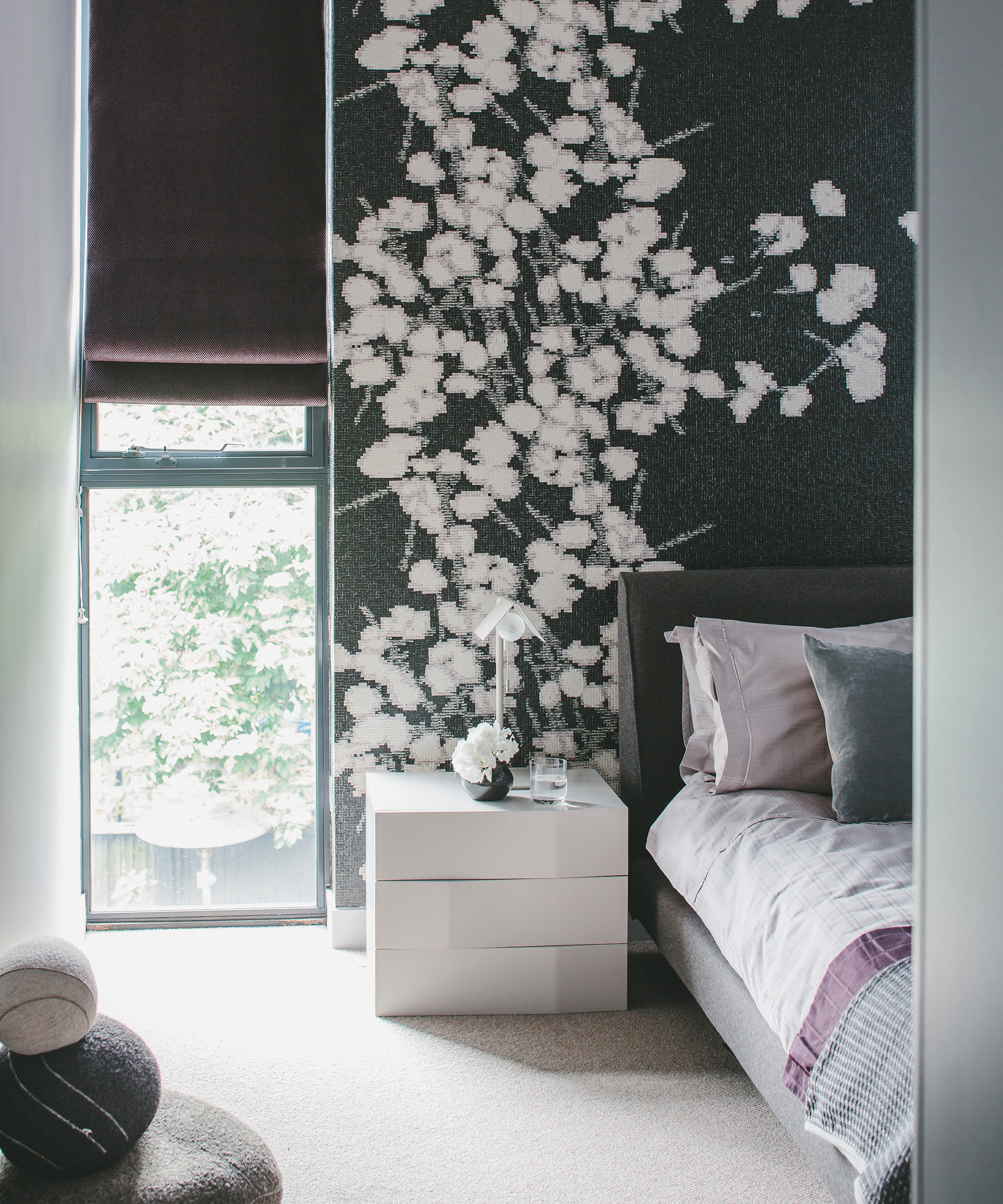 A bedroom with a floor to ceiling window next to a black and white floral wall mural