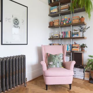 Living room with wooden flooring, a red and white striped armchair, bookshelf, and cast iron radiator on the white wall