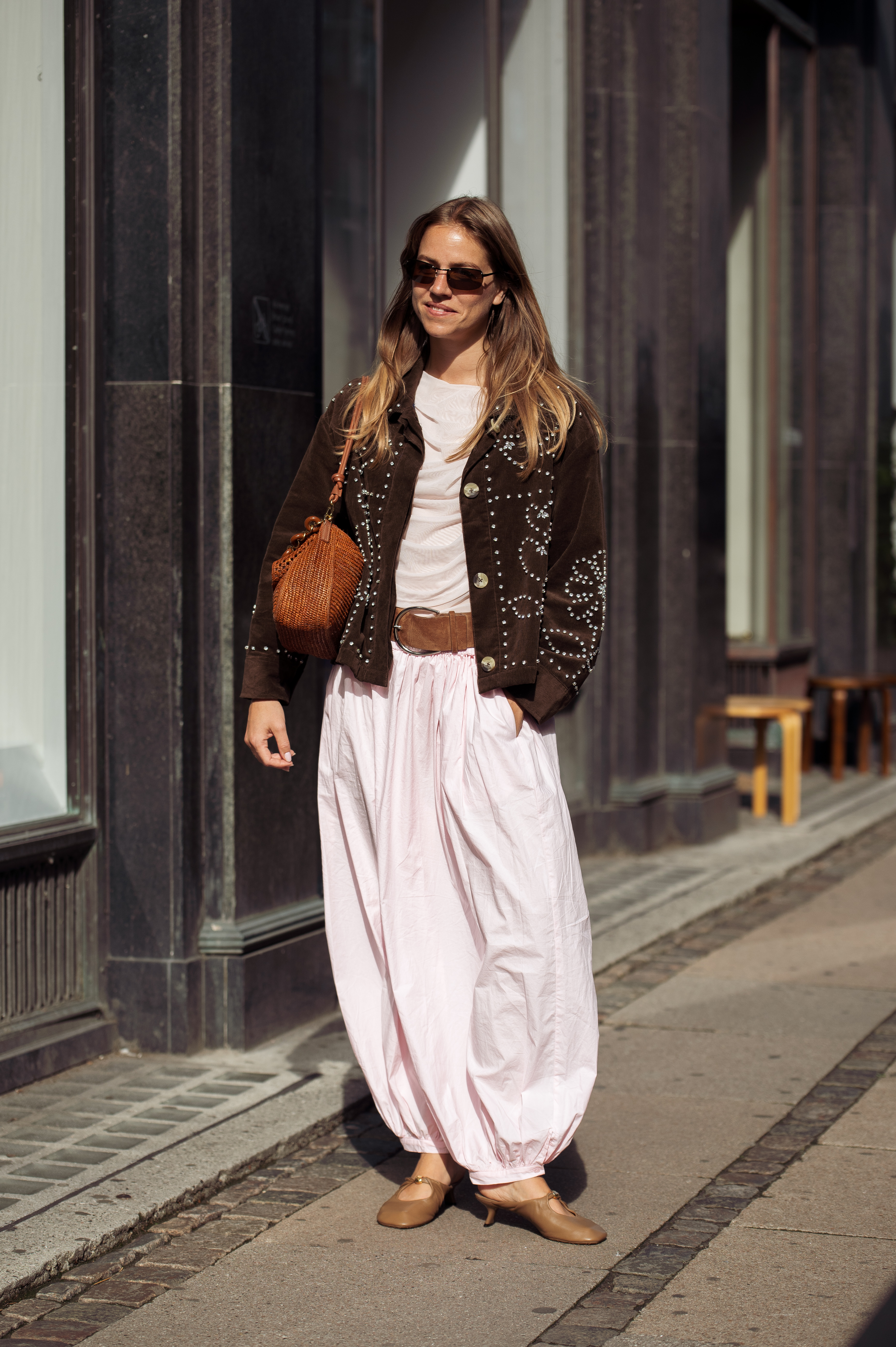 A fashion person spotted in Copenhagen wears the pale pink trouser trend. She paired her trousers with a matching draped top, a swing low suede belt and raffia bag and a Western suede jacket in a recent image taken from Getty.