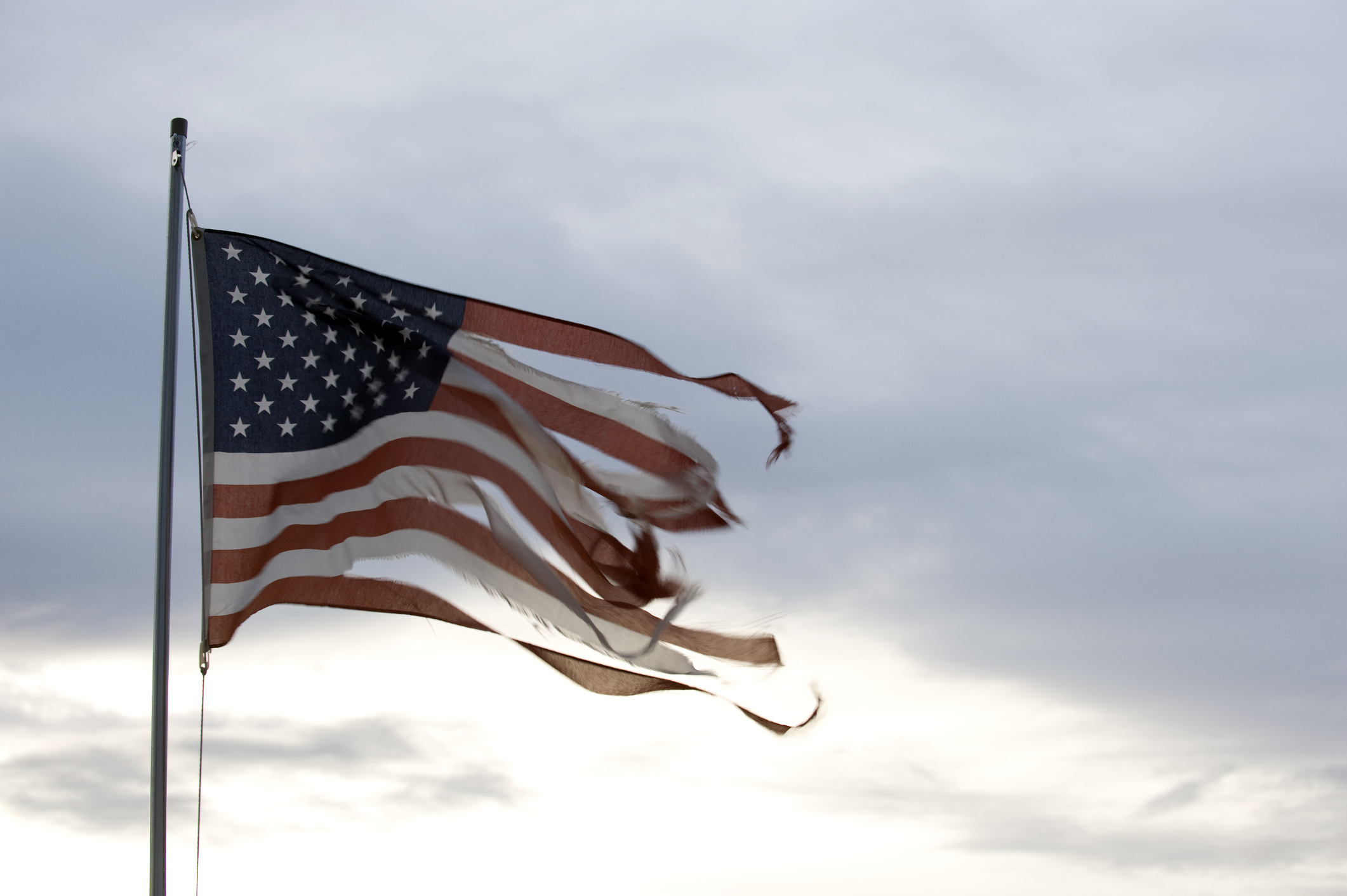 The American Flag being torn to pieces by strong winds. Storm clouds in the background