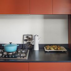 Gas stove with blue Le Creuset cast iron pot on top, red kitchen cabinets and black worktop