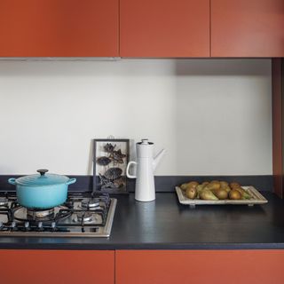 Gas stove with blue Le Creuset cast iron pot on top, red kitchen cabinets and black worktop