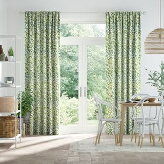 White dining room with leaf print curtains and a wooden dining table