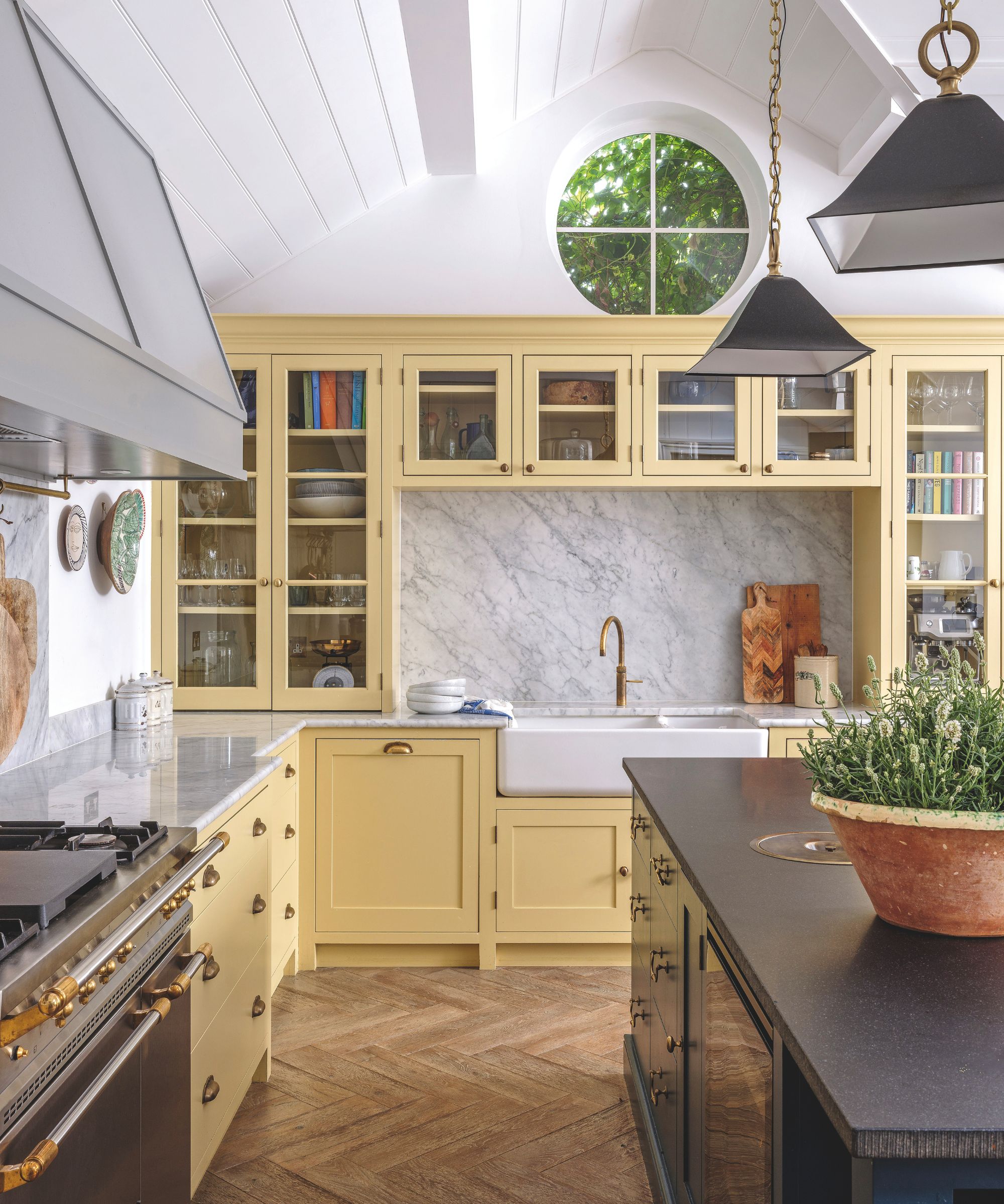 A farmhouse-style kitchen with pale yellow cabinetry, a white farmhouse sink, marble backsplashes, and a dark kitchen island.