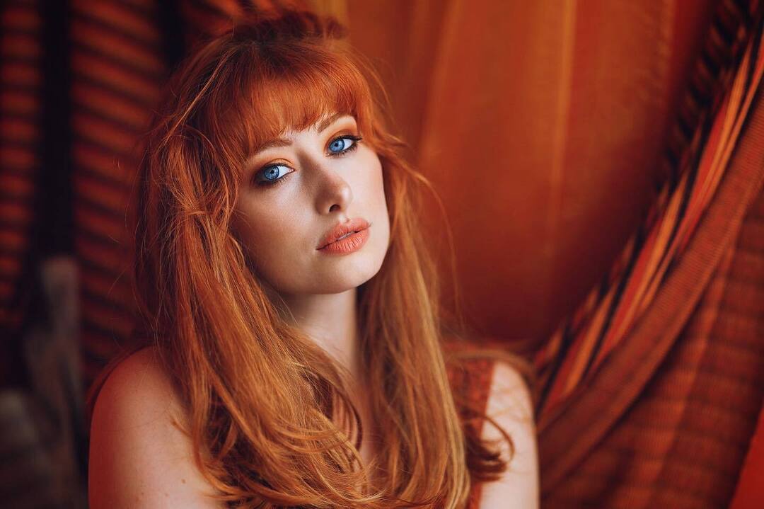 Portrait of a redheaded woman in front of burnt orange curtains