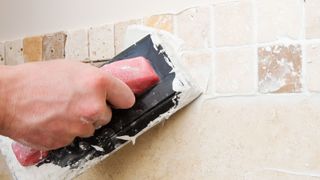 Hand holding grouting trowel on tiled wall applying grout