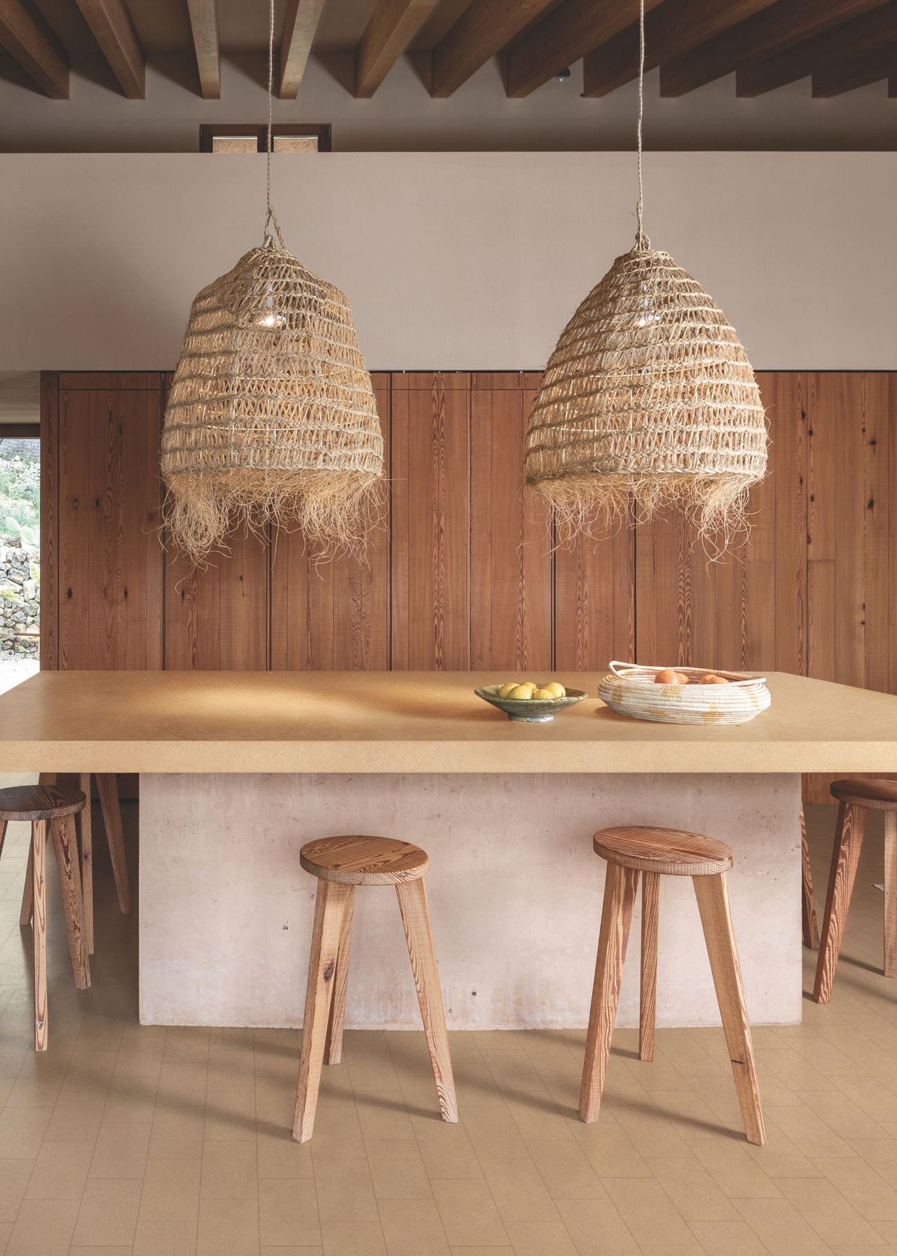 A kitchen with an island and bar stools. Above the island are pendant lights
