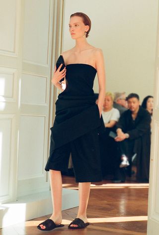 a photo of a model wearing an all-black outfit with slide sandals from the minimal fashion brand the row