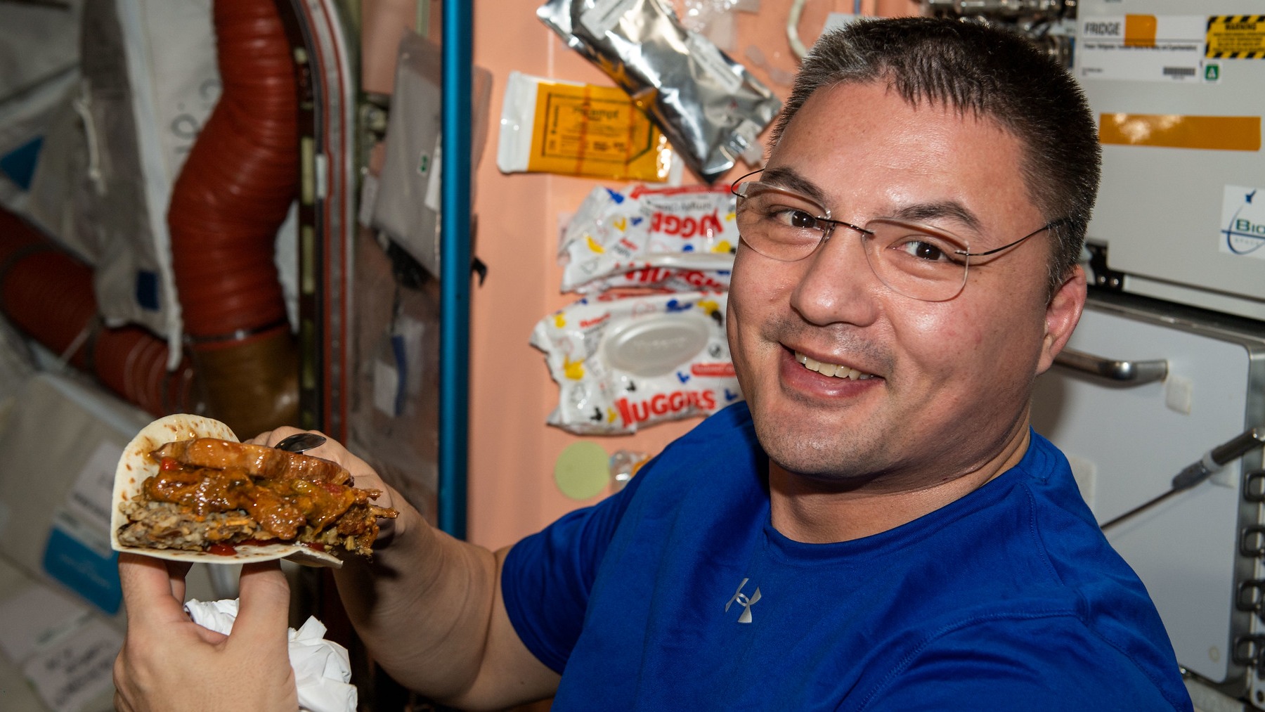crew-4 astronaut kjell lindrgen holds an absolutely overstuffed tortilla filled with layers of meat and other ingredients