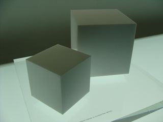 A small and large cube in dark colour under a neon light.