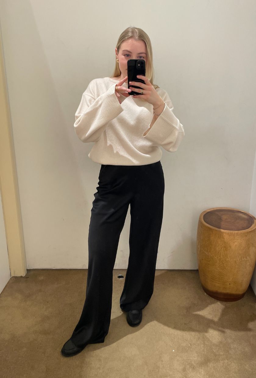 Woman wears cream knit, black trousers and loafers