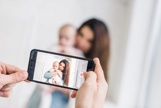 Mum holding baby while posing for a photo being taken on a smartphone