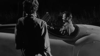 A woman approaches a man in a convertible car in Kiss Me Deadly