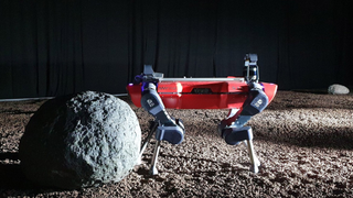 red robot with a rock at the left, on a simulated plain of regolith