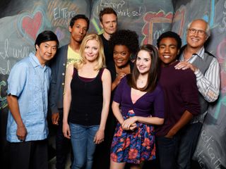 a promo shot for the show Community of the cast all smiling and standing together in front of a chalk board