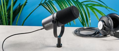 the shure mv7i, a black microphone with a black muff, touch LED pad, XLR connection and TRS input and USB-C input at the rear, photograhped against a blue tom&#039;s guide background with a pair of over-ear wired headphones 