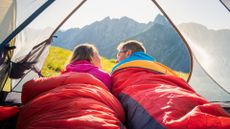 A man and woman in a sleeping bag in a tent