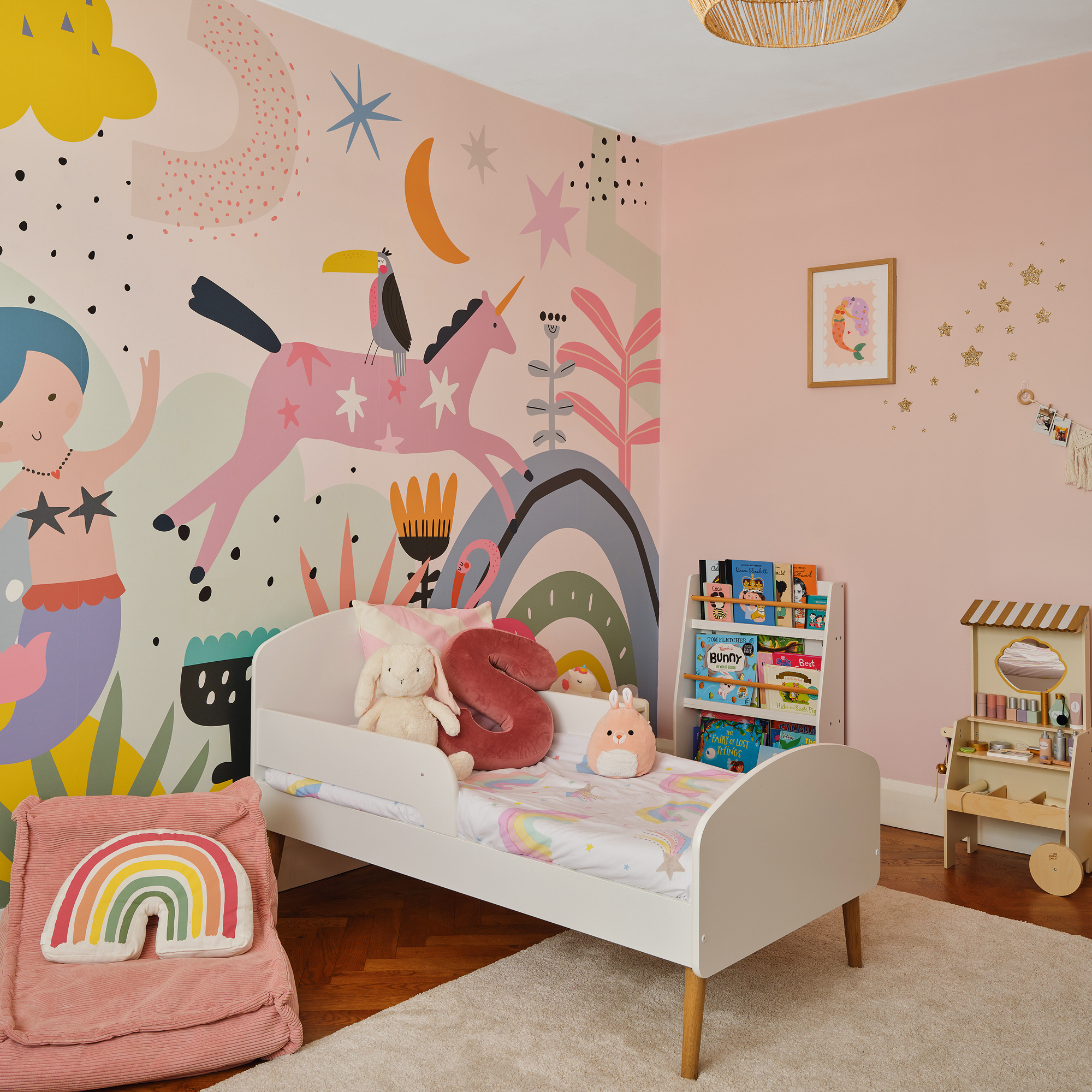 a child's bedroom with pink walls and. a large mural with cartoon mermaid and unicorn