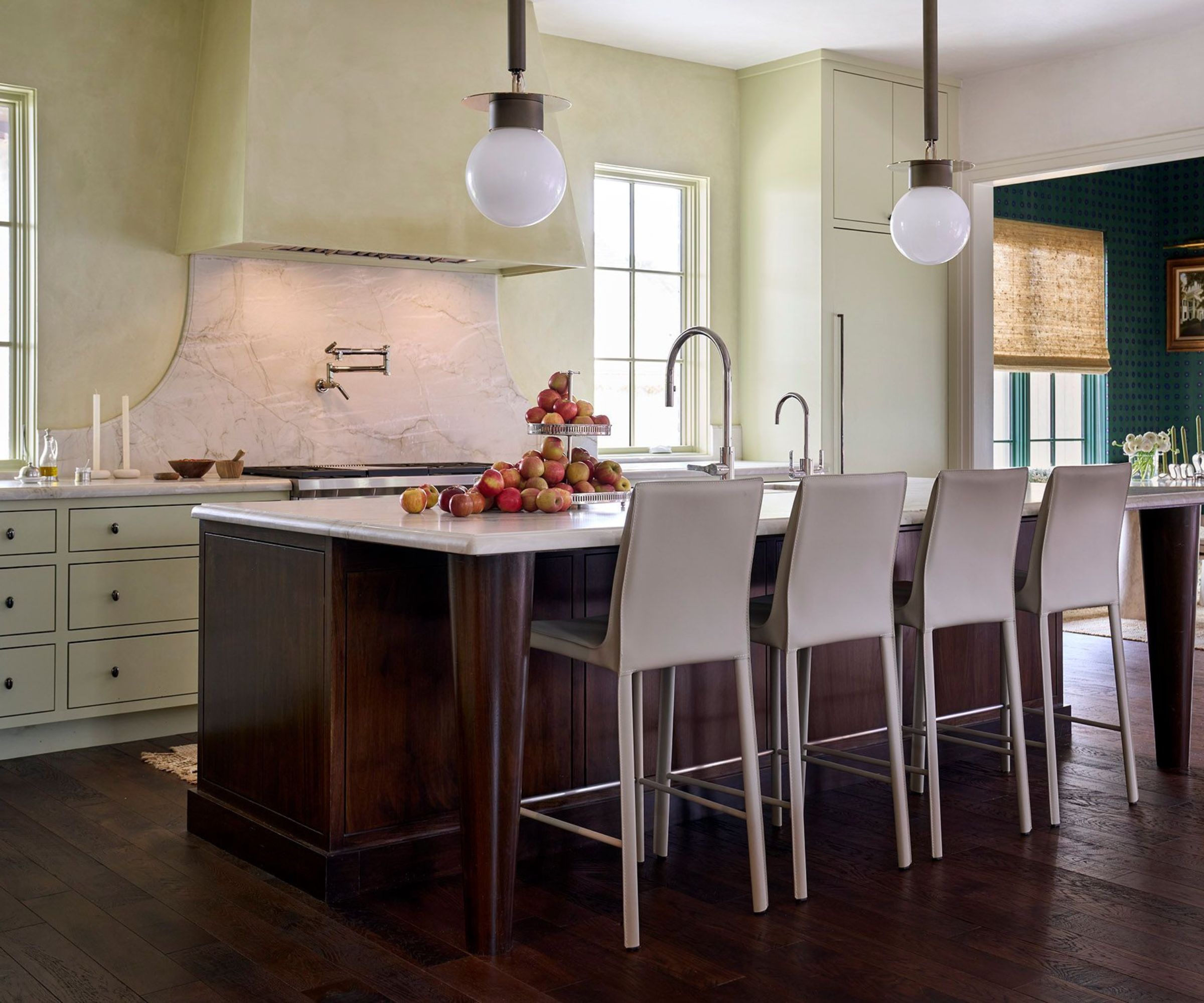 A large kitchen with dark wood flooring, a walnut wood kitchen island with white countertops, pale green walls, and matching cabinets.