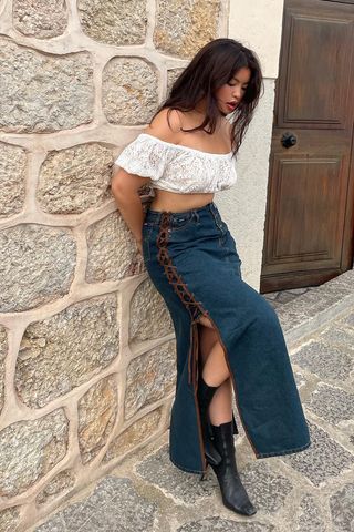 a photo of a woman wearing brown heeled ankle-boots in summer with a denim high-slit skirt and cropped white puff-sleeve top