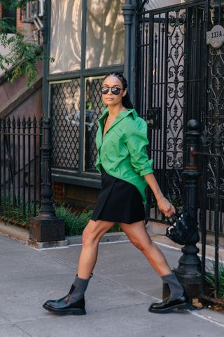 a photo of a woman wearing black ankle-boots in summer with a black mini skirt and a green button-down shirt