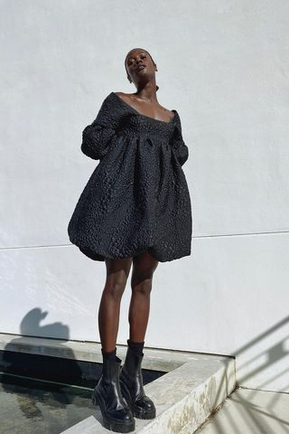 a photo of a woman wearing black chelsea ankle-boots in summer with a black puff sleeve baby doll dress